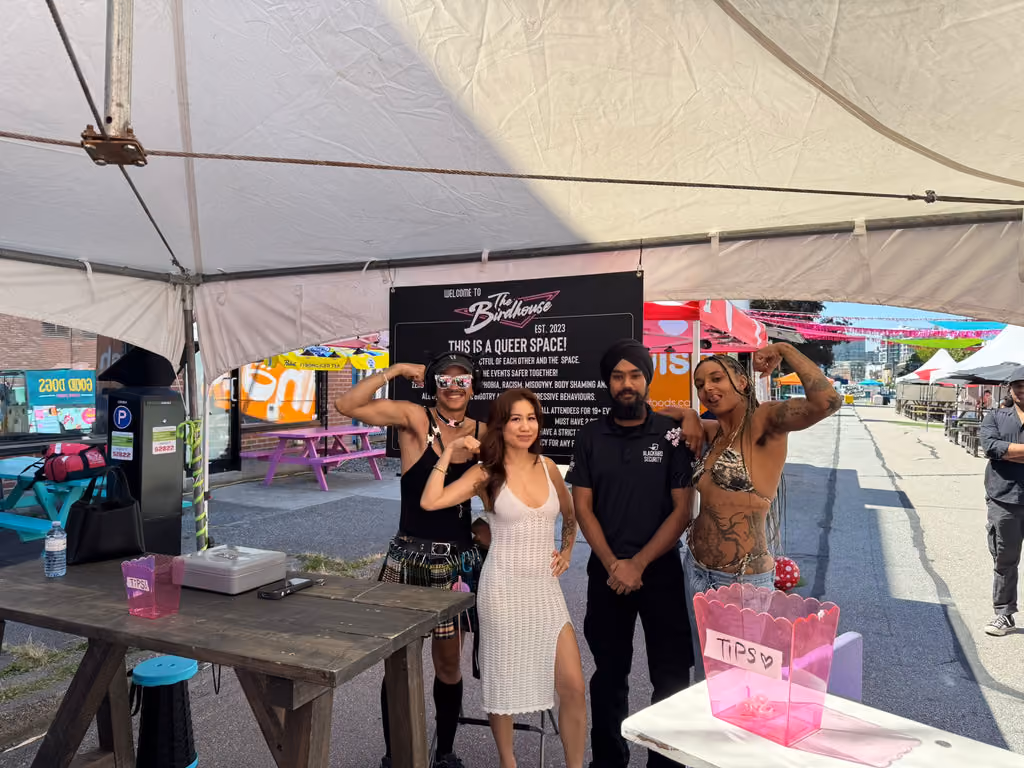A Blackbird Security guard stands under a tent with LGBTQ+ people at an event at The Birdhouse in Vancouver during Pride weekend.