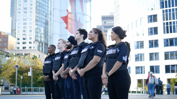Five Blackbird security guards standing in a row looking out over street