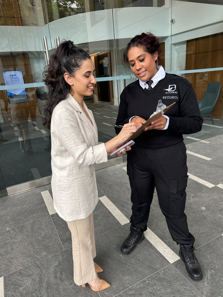 Uniformed Blackbird security guards standing with clipboard in hand speaking to woman