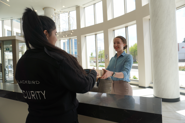 Uniformed Blackbird security guard handing a woman a package at reception desk