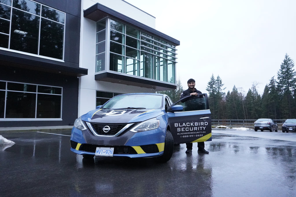 Uniformed Blackbird security guard in front of Mobile patrol car