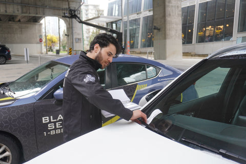 Uniformed Blackbird security guard placing parking ticket on car window