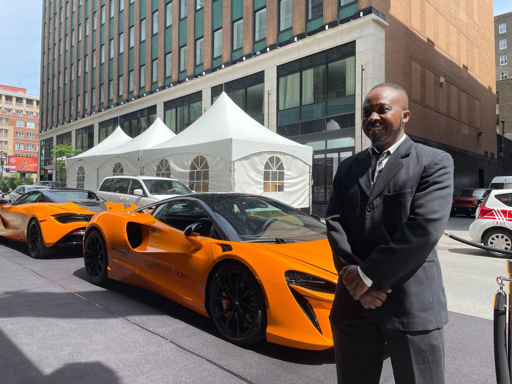 A suit and tie security guard stands in front of a row of McLarens at a high-end event in Montreal.