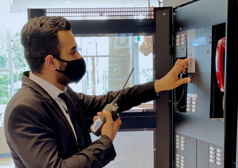 Blackbird security guard pushing button at control panel with radio in hand