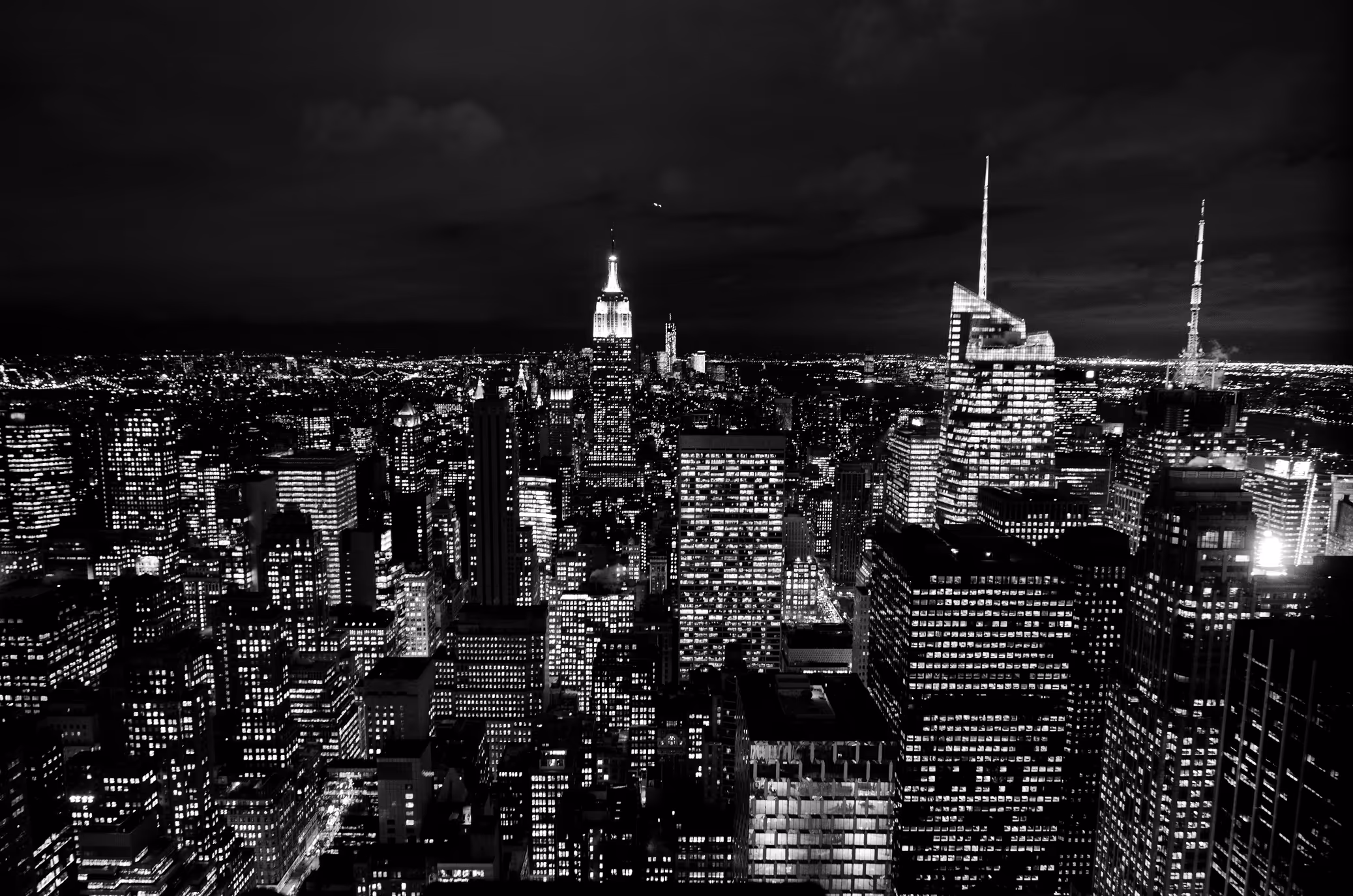 Black and white night view of a city skyline with illuminated skyscrapers, including the Empire State Building.
