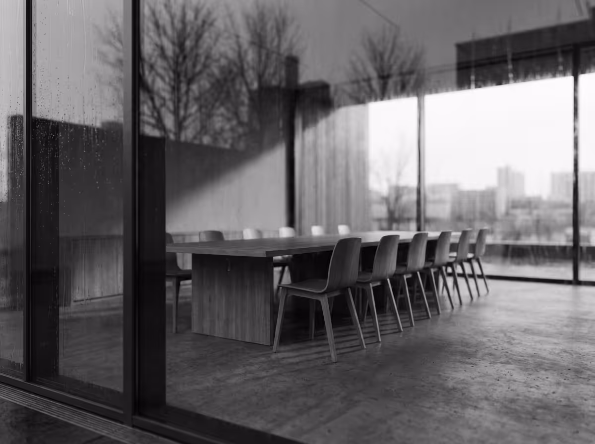 Empty modern conference room with a long wooden table and several wooden chairs, viewed through rain-speckled glass walls.