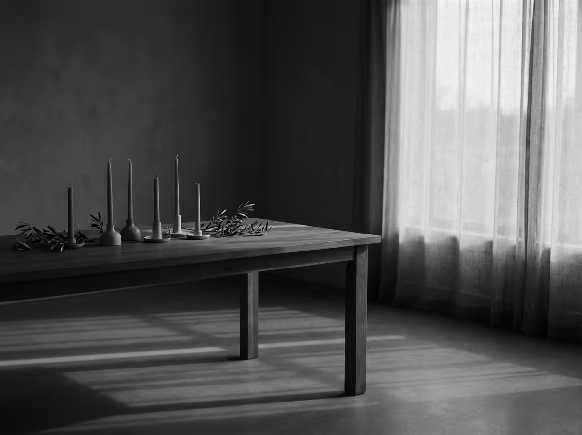 Wooden table with six unlit candlesticks and green leaves near a window with sheer curtains casting shadows on the floor.