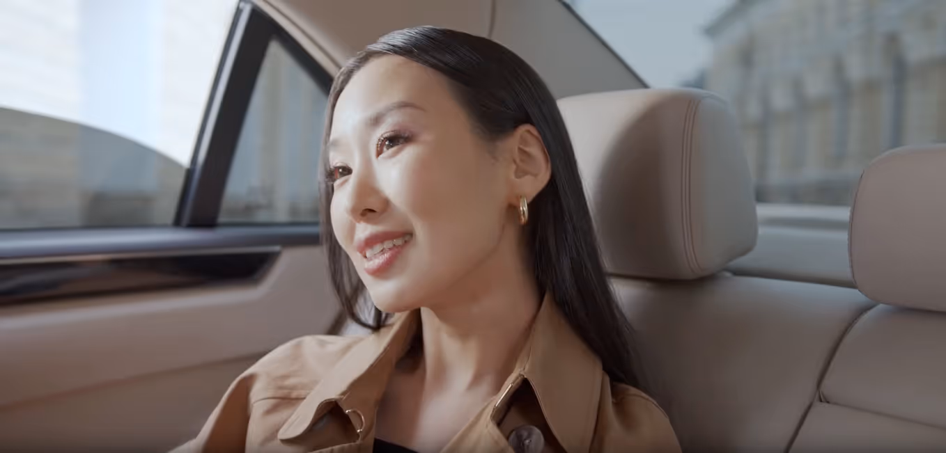 Woman with long dark hair smiling and sitting in the backseat of a car with beige leather seats.