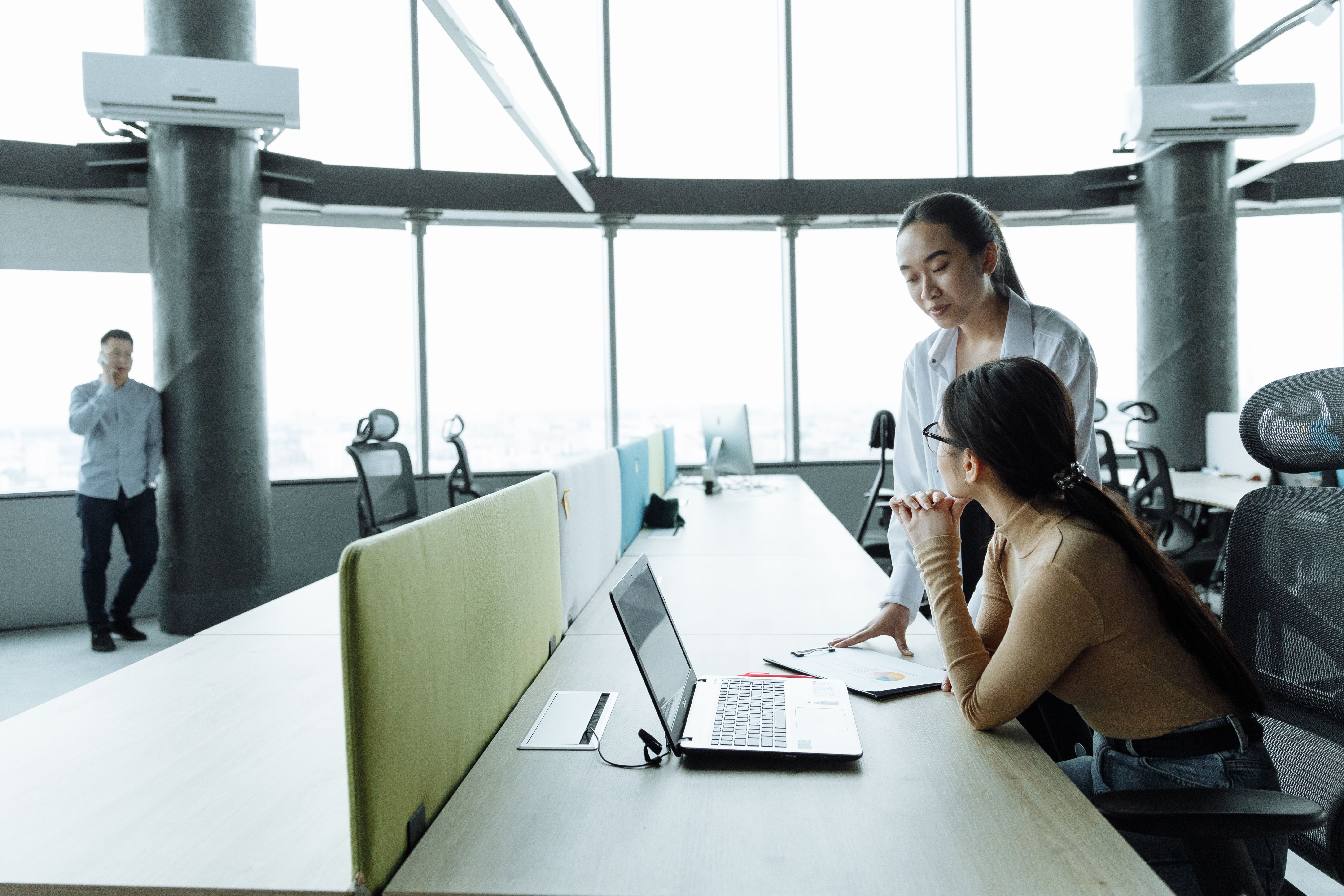 Two colleagues reviewing work on a laptop in an open plan office