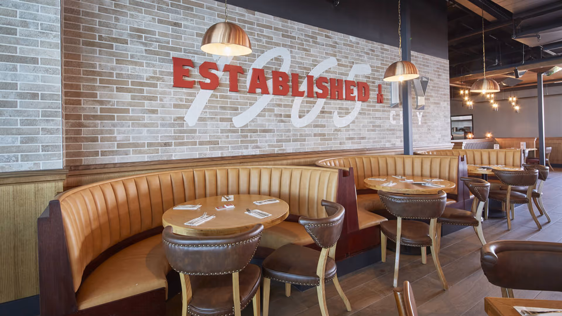 Modern kitchen with dark cabinetry, gray marble island with three black bar stools, and a vase of greenery on the countertop.