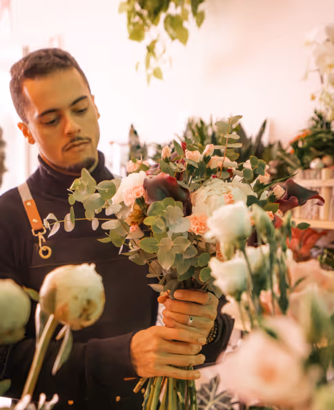 Man arranging a bouquet of assorted flowers and greenery inside a flower shop.