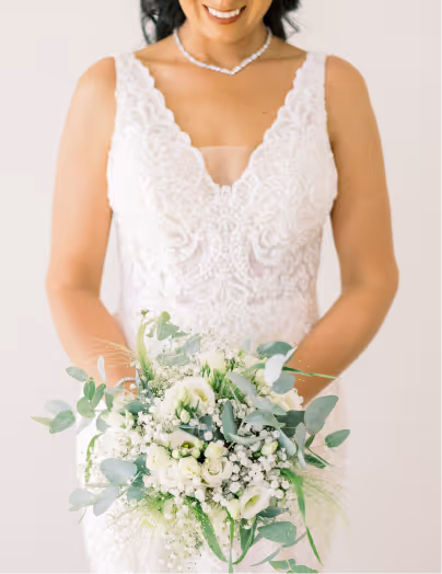 Bride in a white lace wedding dress holding a bouquet of white flowers and greenery.
