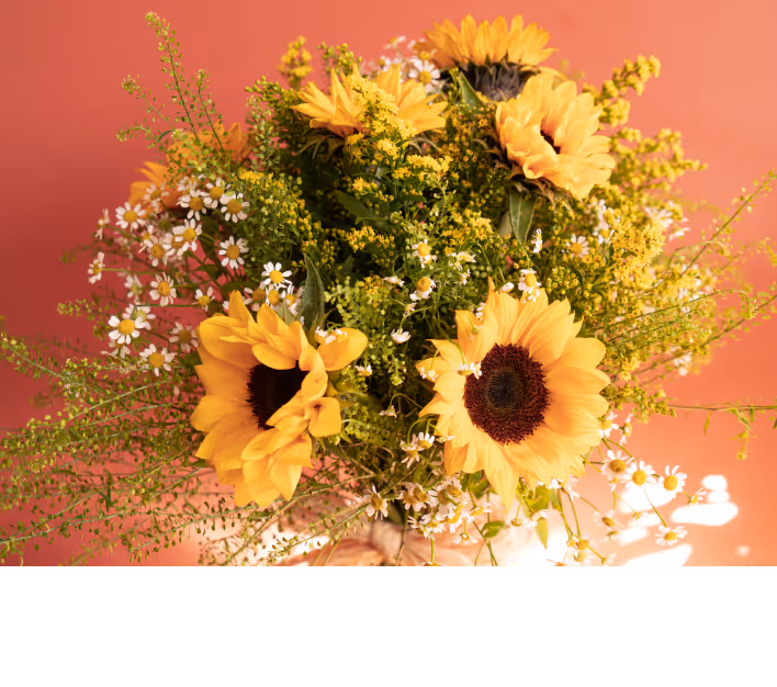 Bouquet of yellow sunflowers mixed with small white daisies and green foliage against a warm orange background.