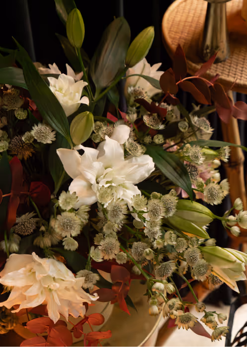 Bouquet of white lilies and small white flowers with green leaves and red foliage on a wooden surface.