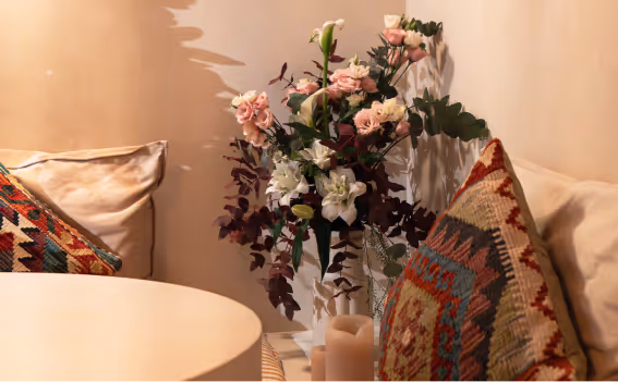 Cozy seating area with a round white table, patterned cushions, and a floral arrangement in a vase next to candles.