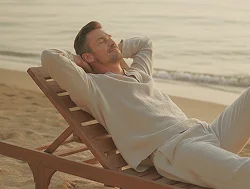 Mann lehnt entspannt auf einem Liegestuhl am Strand mit geschlossenen Augen.