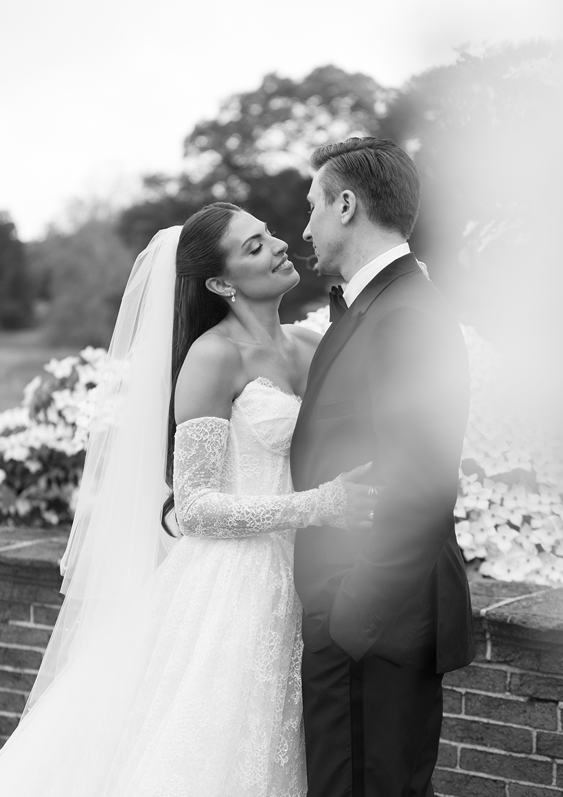 Bride and groom embracing and looking at each other outdoors in a garden setting, in black and white.