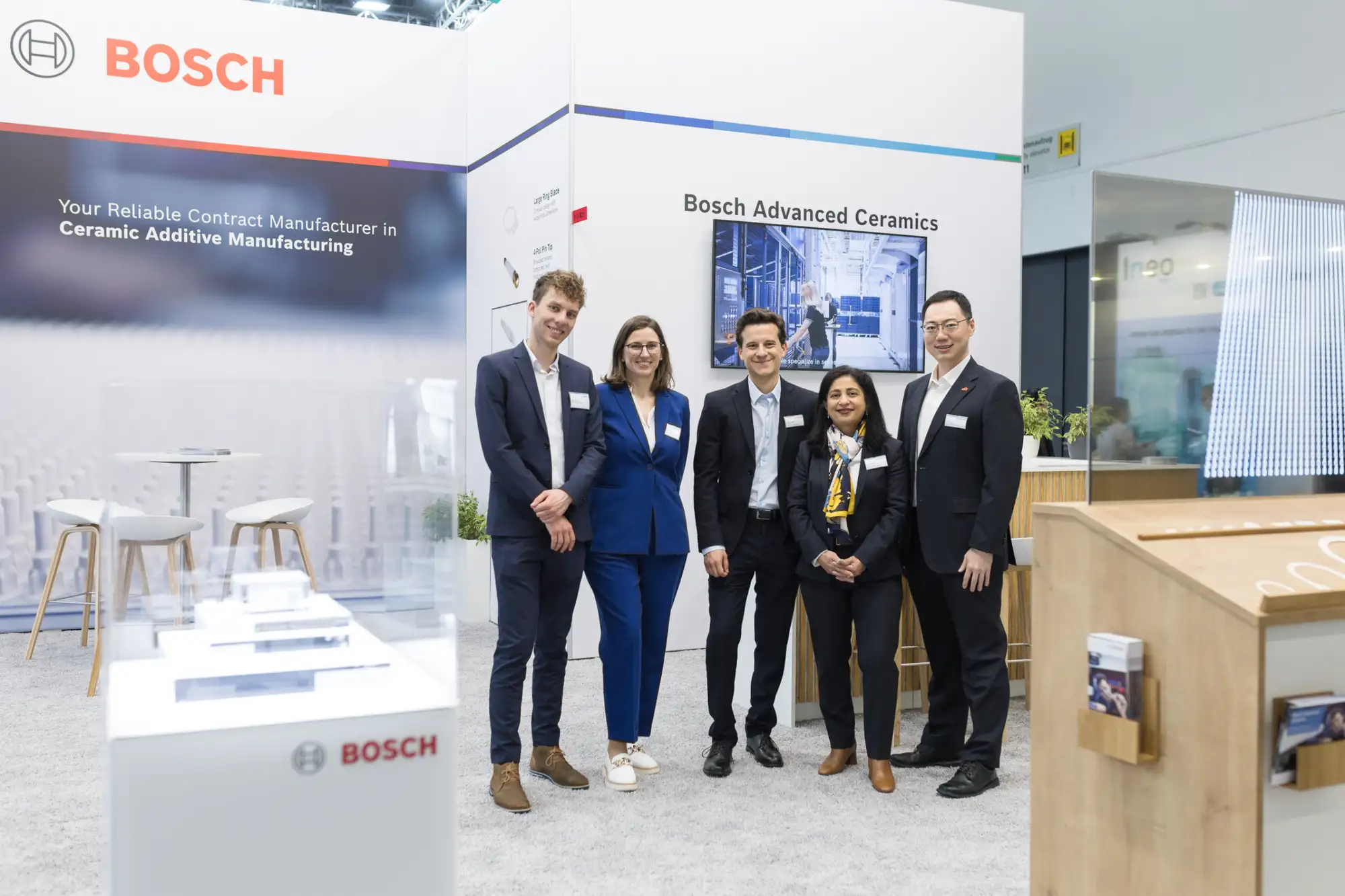 Five professionals posing at Bosch booth promoting ceramic additive manufacturing at an exhibition.
