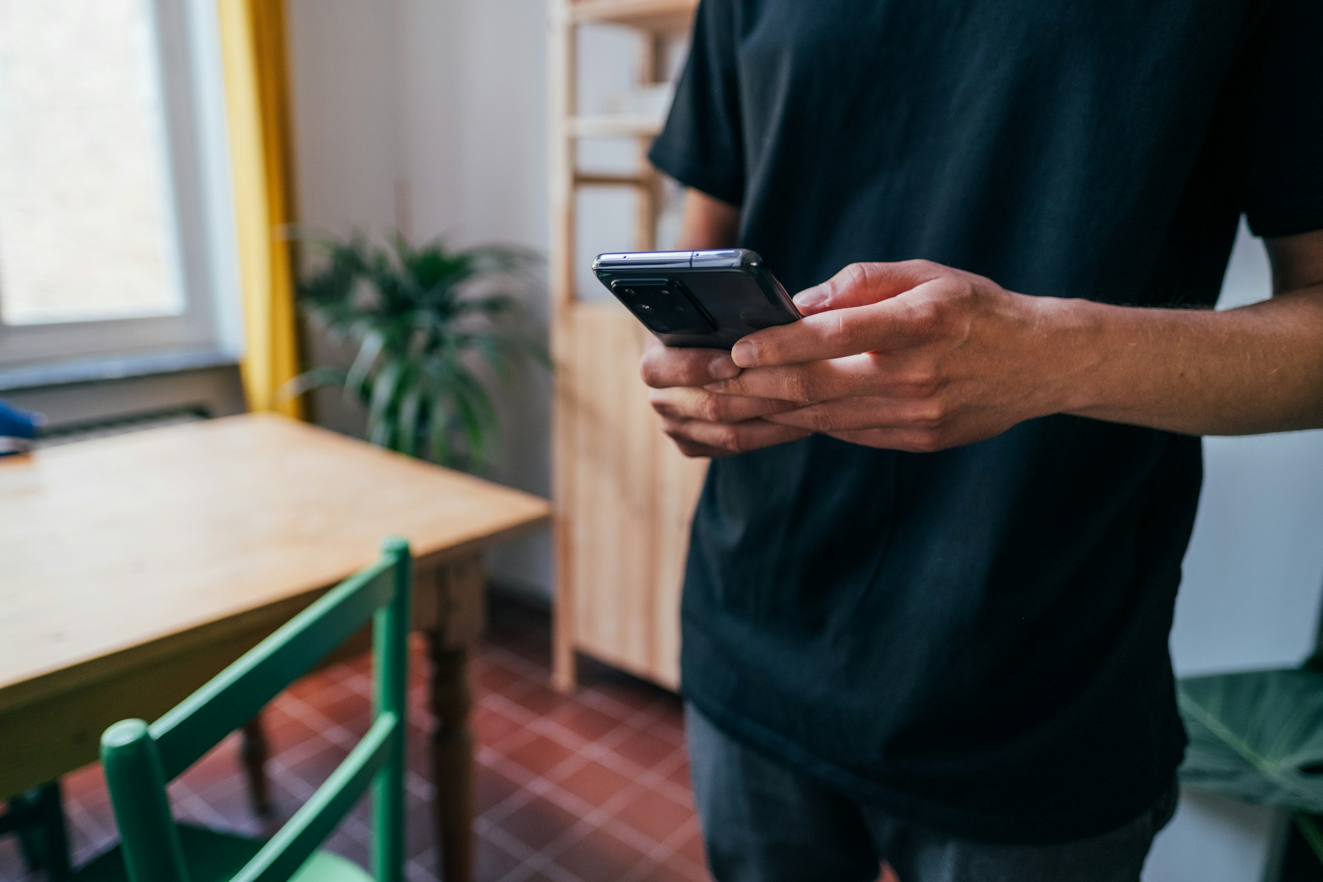 A close-up of a person's hands holding a dark smartphone with a clear case in a bright setting, with a glimpse of a table and shirt fabric.
