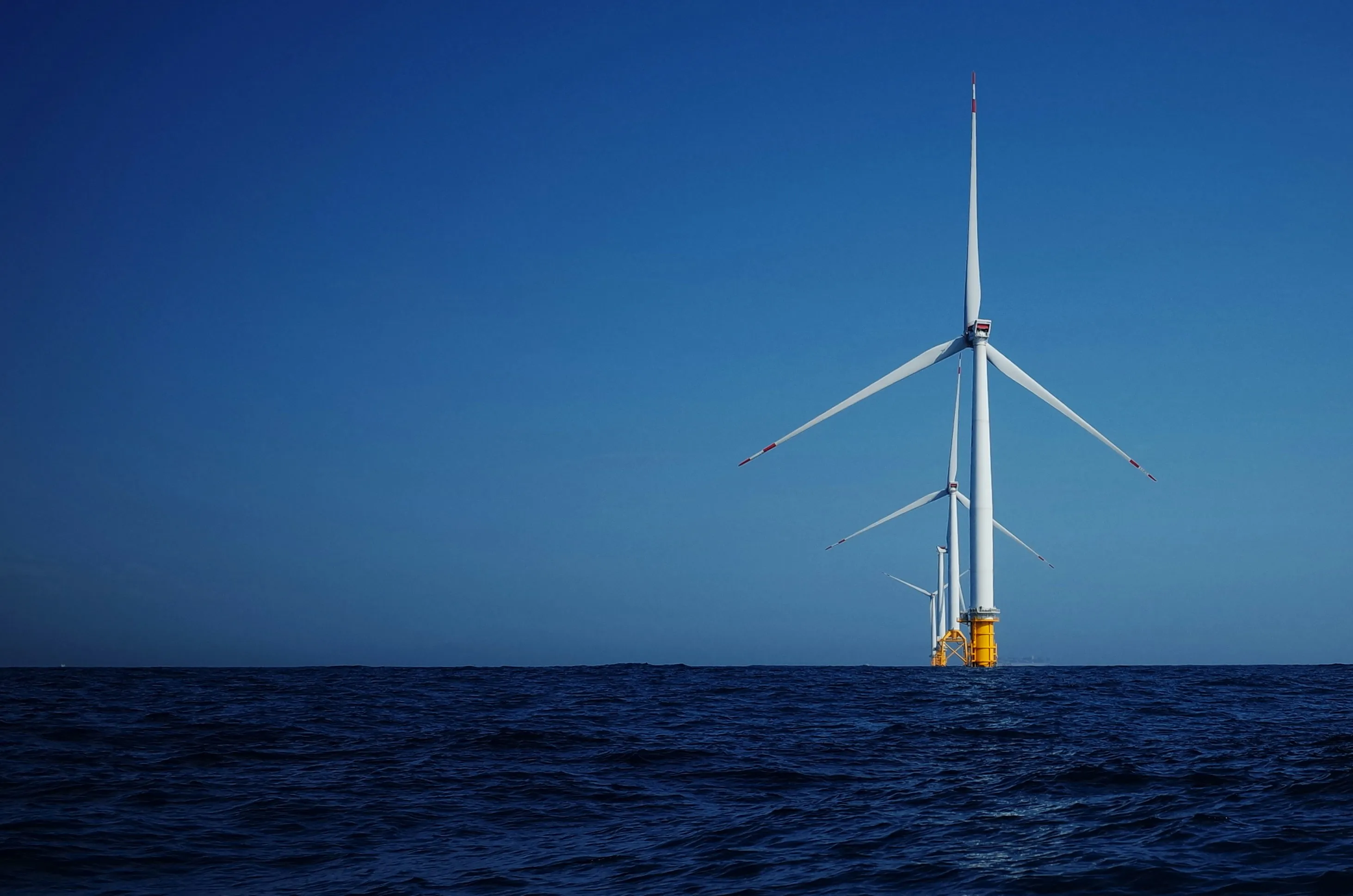 Series of offshore wind turbines with yellow bases in the ocean under a clear blue sky.