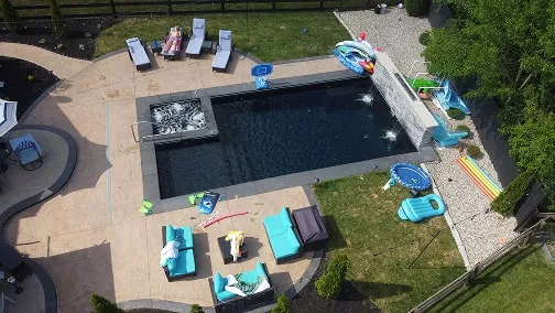 Aerial view of a backyard with a rectangular pool, lounge chairs, pool toys, and turquoise outdoor seating on a patio.
