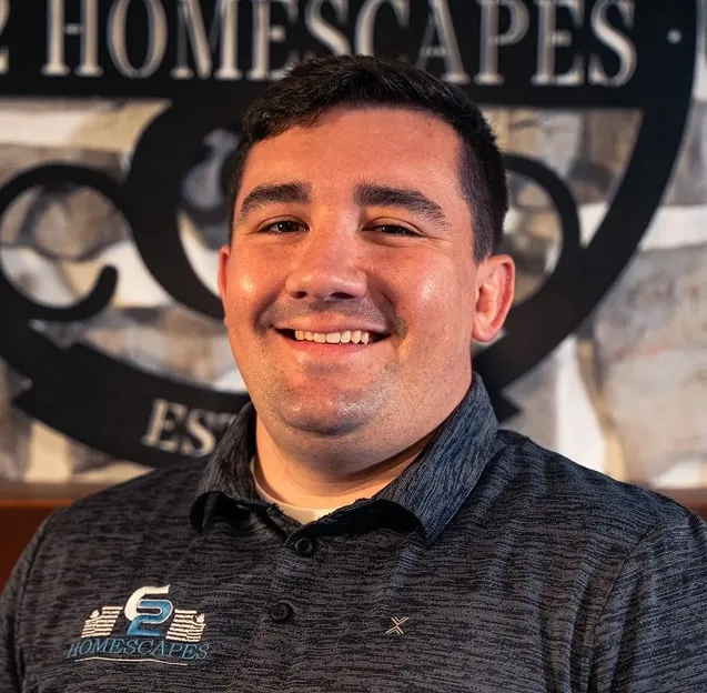Smiling man wearing a dark blue Homescapes polo shirt in front of a Homescapes logo wall.