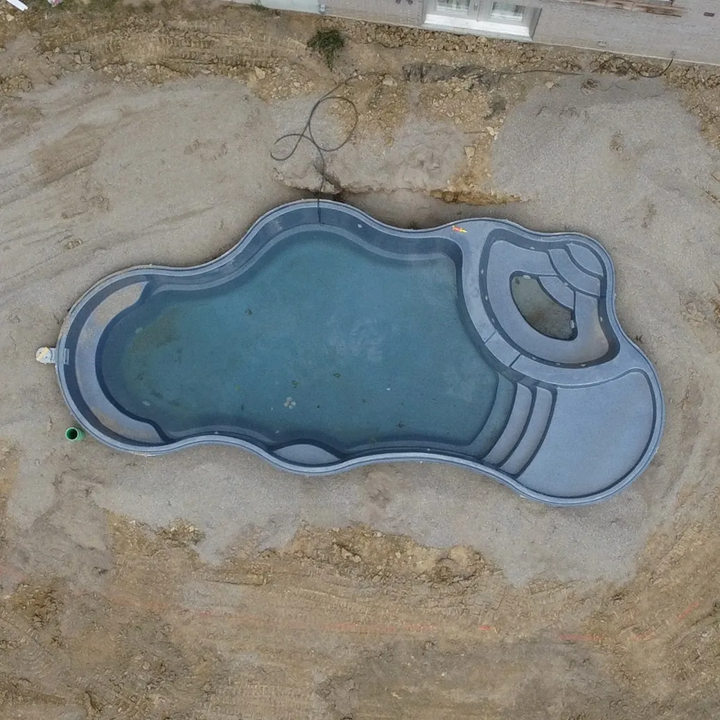 Aerial view of an empty irregular-shaped swimming pool surrounded by dirt and construction ground.