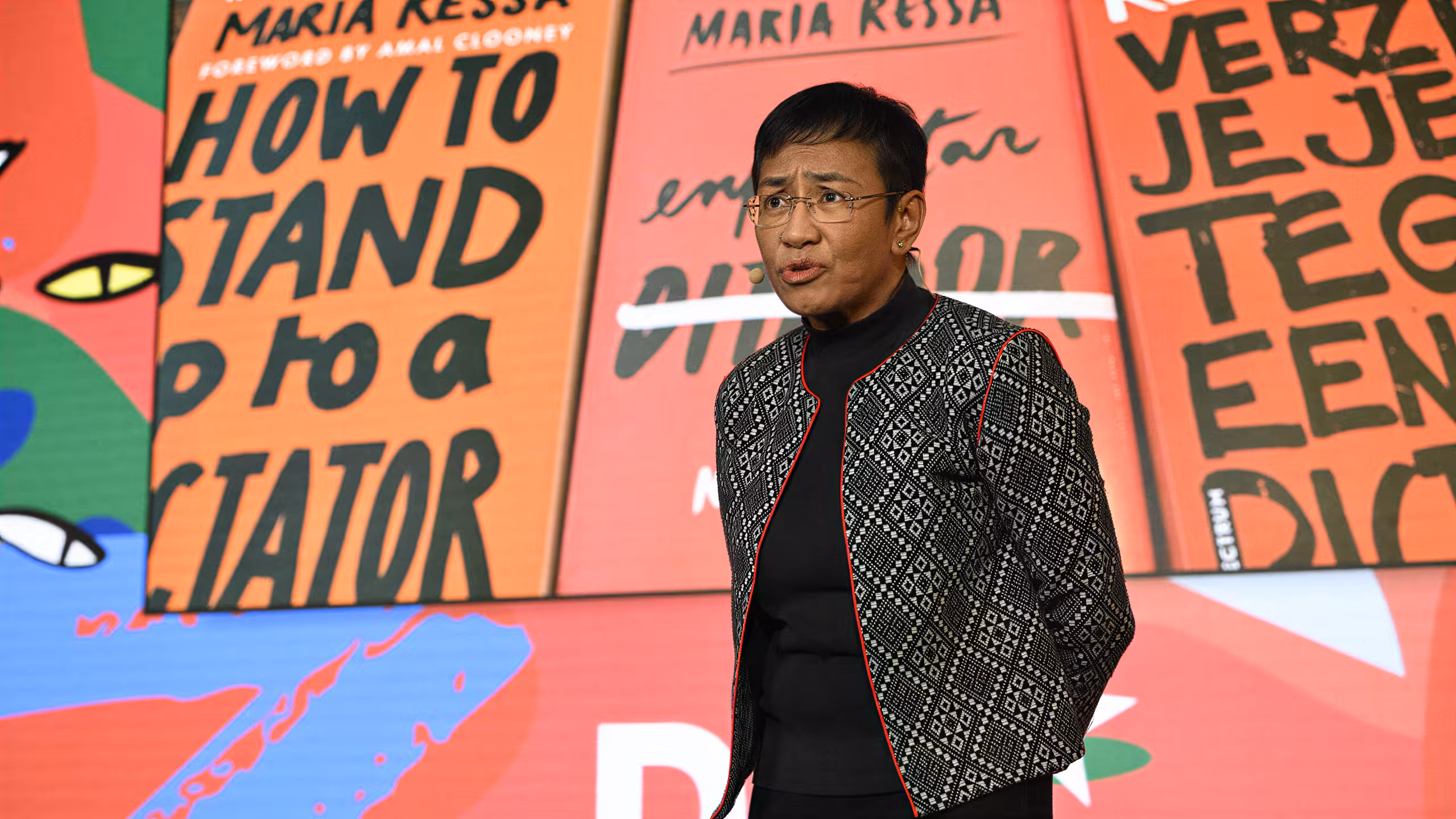 Journalist and Nobel Laureate Maria Ressa standing in front of a colourful animated background giving a keynote speech