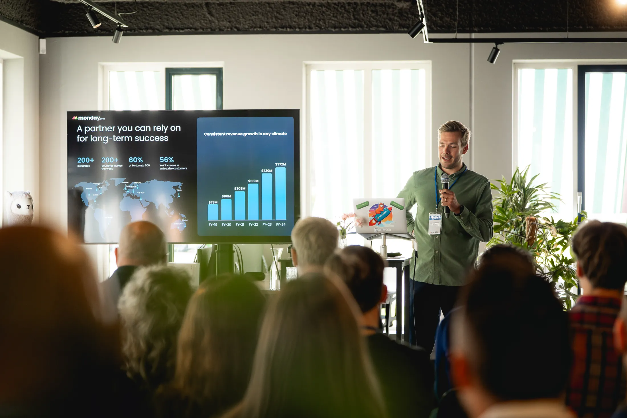 Open laptop en notitieboek op houten bureau in modern kantoor met planbord op achtergrond en ochtendlicht door raam.