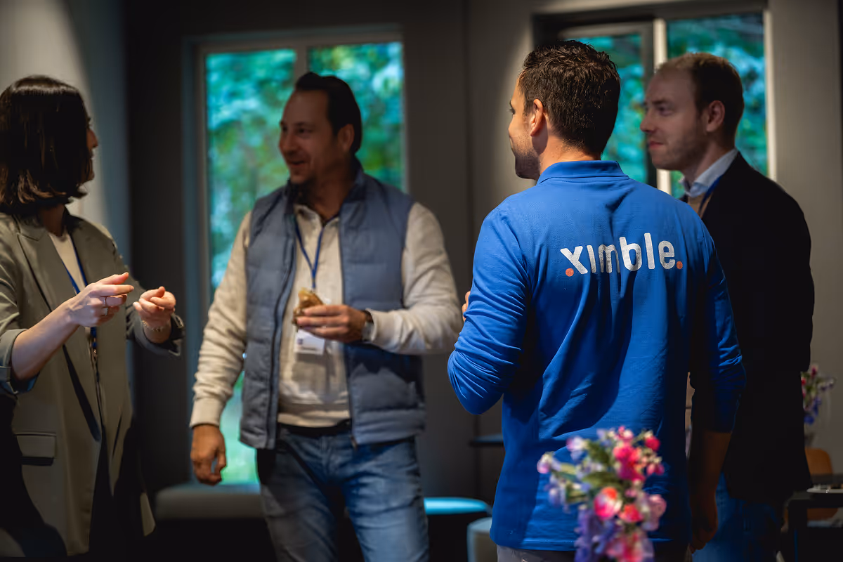 Modern open werkruimte met aparte werkzones voor tech, bouw en zorg, grote digitale takenmonitor op achtergrond, ochtendzon met zachte schaduwen