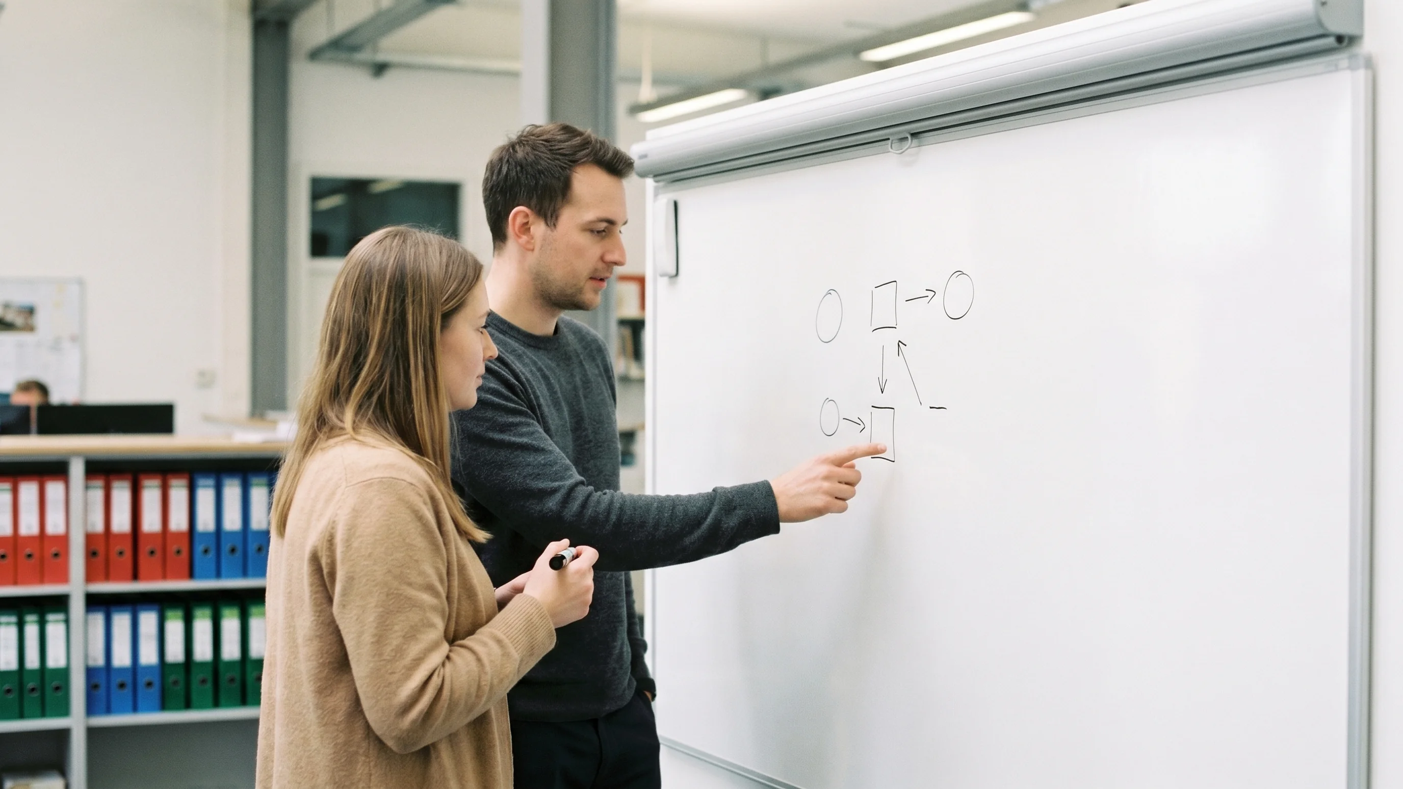 Twee collega's bespreken procesverbetering bij een whiteboard met pijlen en schema's zonder tekst