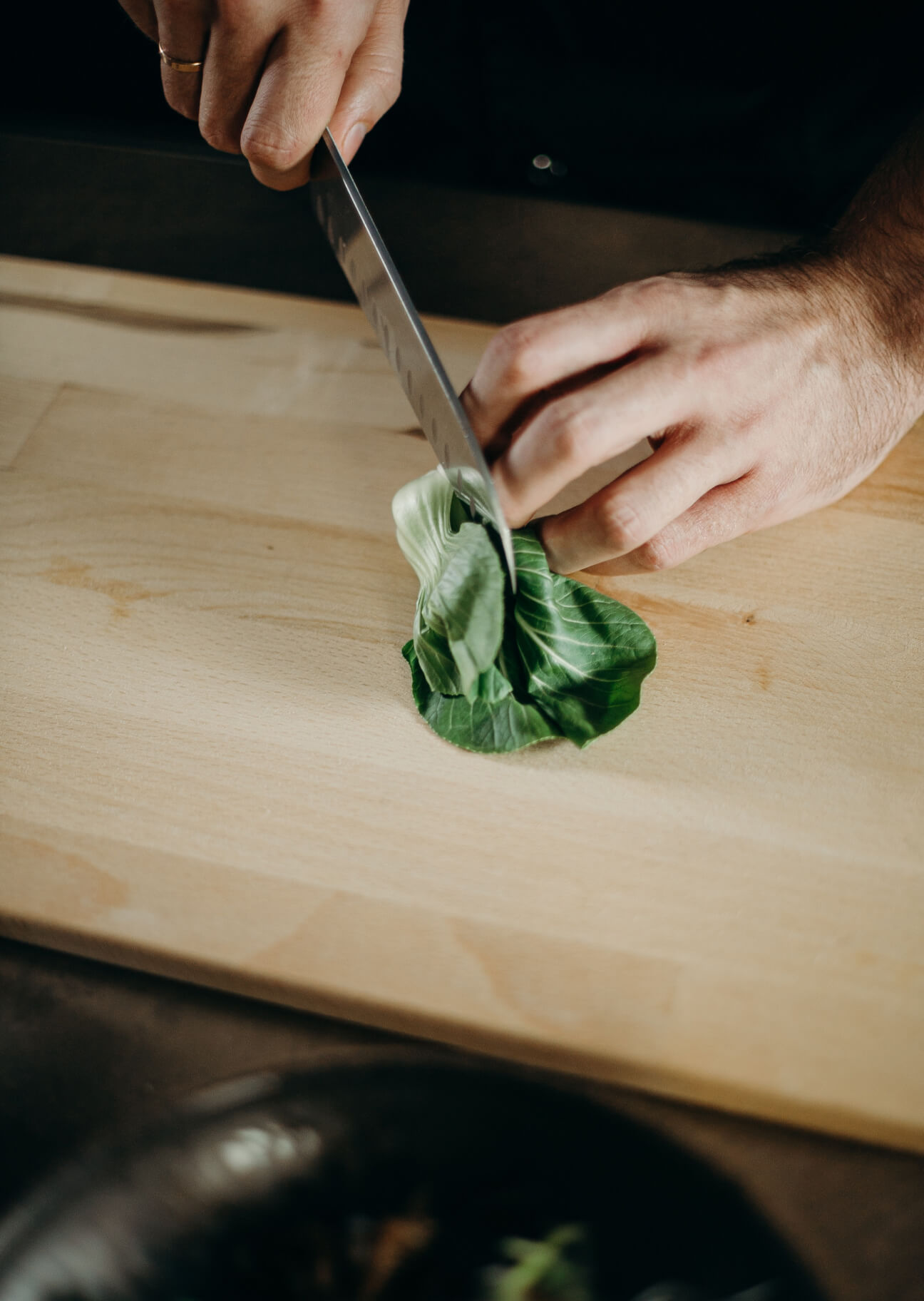 Manos cortando hojas verdes frescas sobre una tabla de madera con un cuchillo.