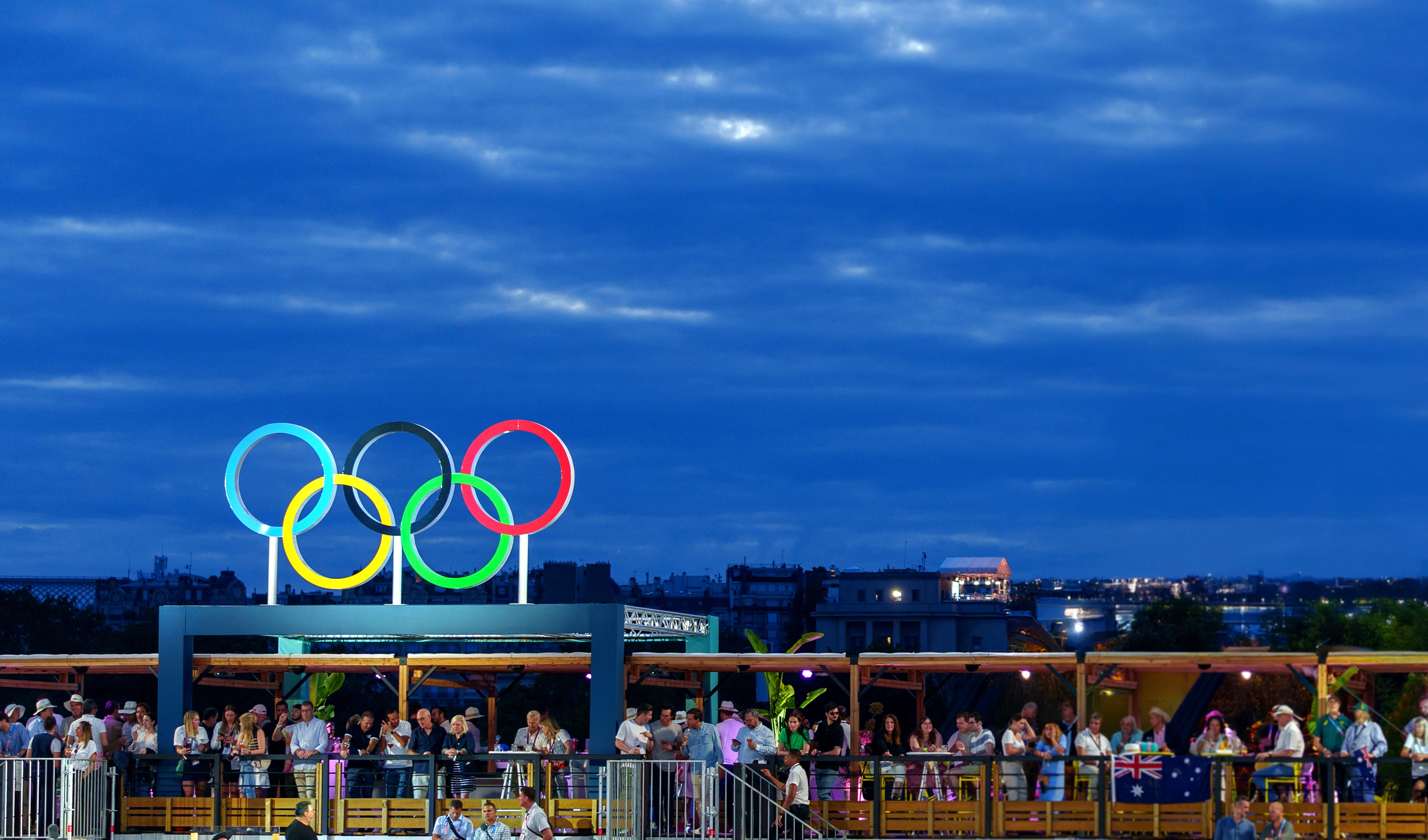 Night time Olympic event with a cloudy sky, people lined up in the rafters to view event. Olympic rings displayed.