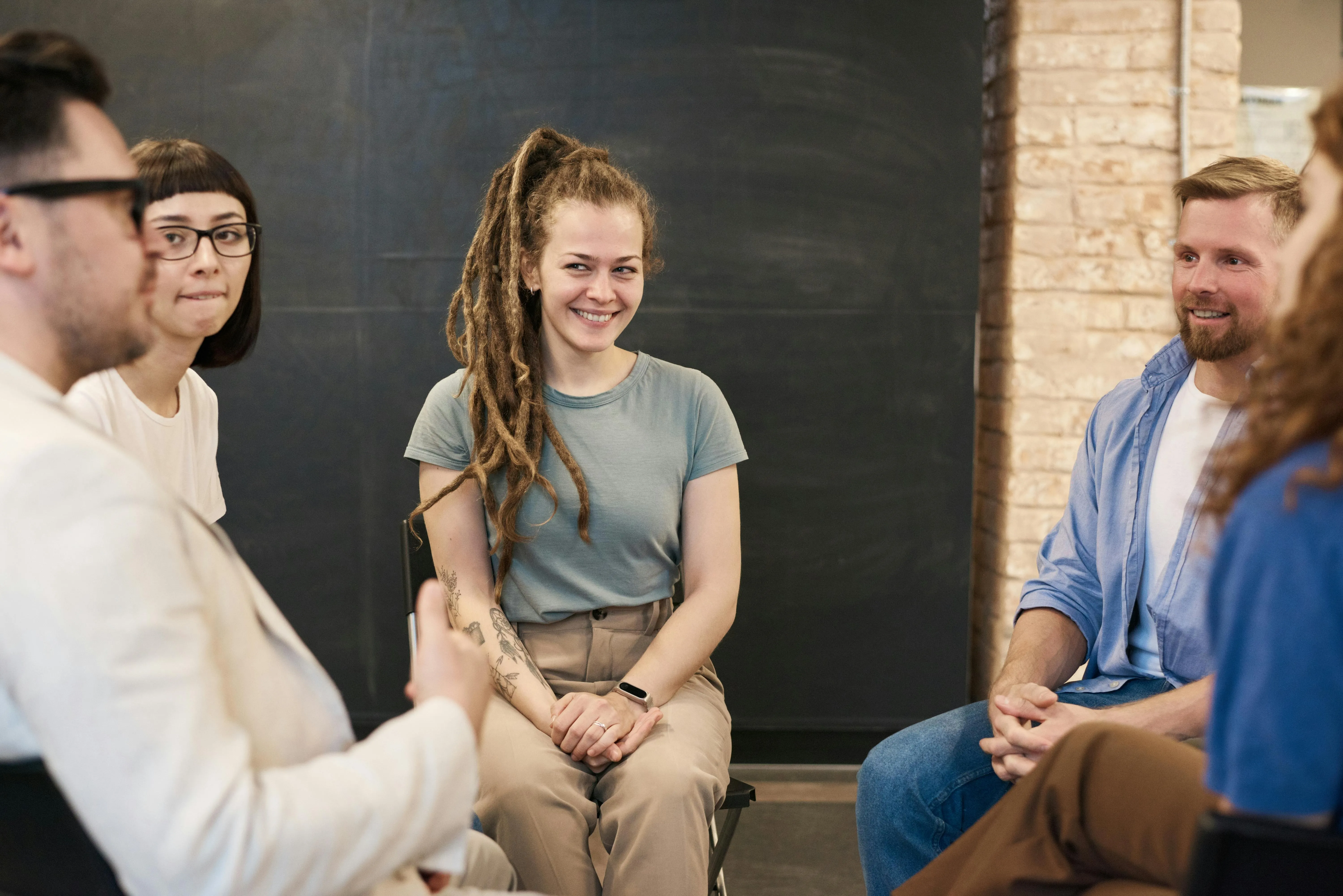 A diverse group of six young adults sitting in a circle and engaging in a discussion in a casual setting.