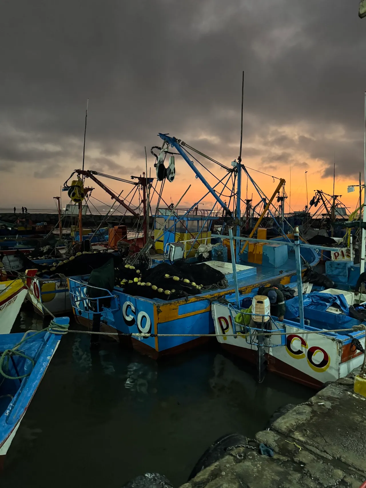 Colorful fishing boats docked at a harbor under a cloudy sunset sky.