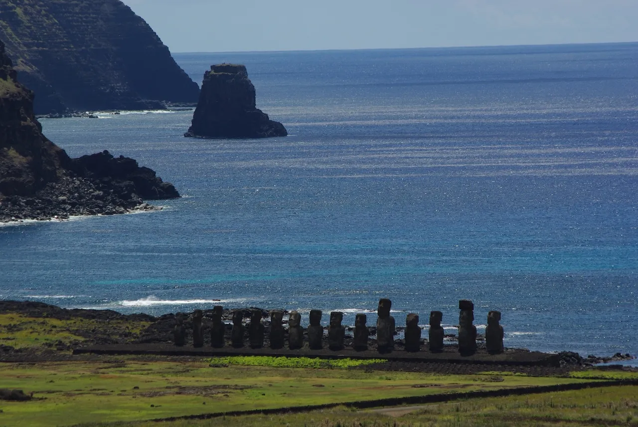 Row of Moai statues on a grassy coastline with blue ocean and rocky cliffs in the background at Rapa Nui National Park.