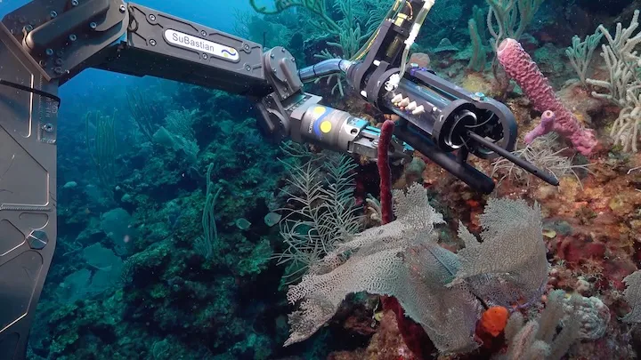 Underwater robotic arm labeled 'SuBastian' reaching towards coral reef with various marine life.