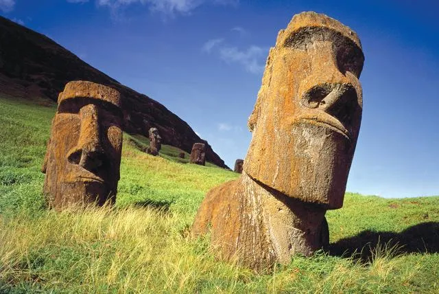 Moai stone statues partially buried in grassy hillside under a blue sky on Easter Island.