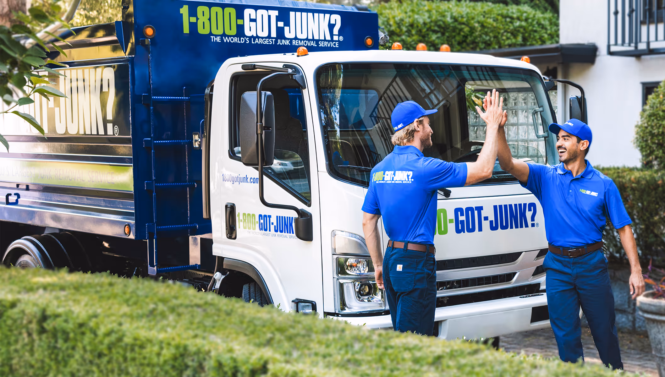 Two 1-800-GOT-JUNK? workers in blue uniforms high-fiving next to a branded junk removal truck.