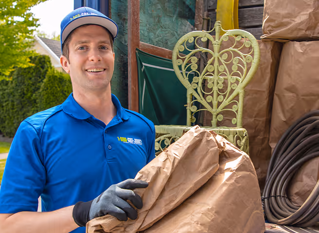 1-800-GOT-JUNK? employee posing by junk removal truck holding brown paper bag