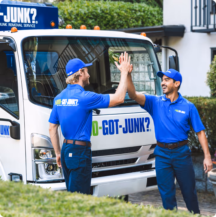 Two uniformed junk removal workers giving each other a high five in front of a 1-800-GOT-JUNK? truck.