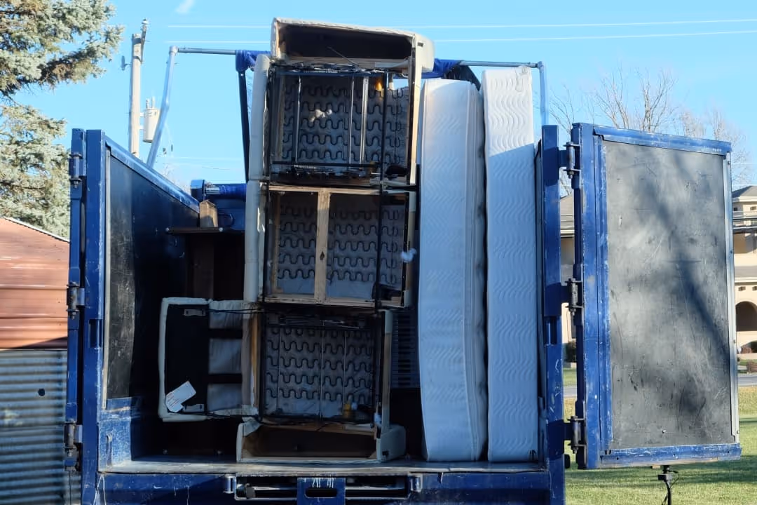 Open 1-800-GOT-JUNK? truck loaded with furniture including mattresses and a couch frame.