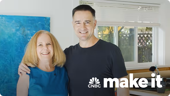 Smiling man and woman standing together indoors near a window, with CNBC Make It logo in the bottom right corner.