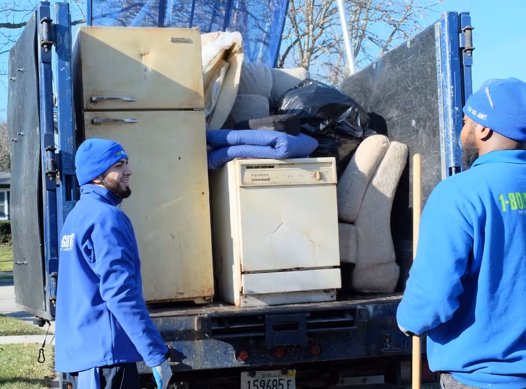 Two movers in blue 1-800-GOT-JUNK? uniforms loading old appliances and furniture into a truck.