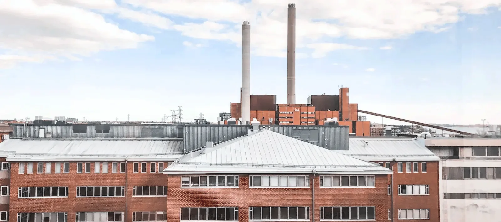 Hattutehtaalta otettu maisemakuva. Punatiilisiä rakennuksia ja Hanasaaren voimalaitois.