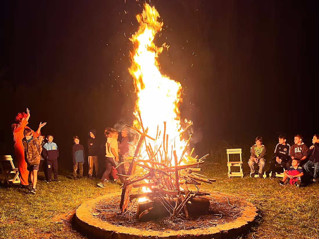 Group of children gathered around a large bonfire at night on grass.