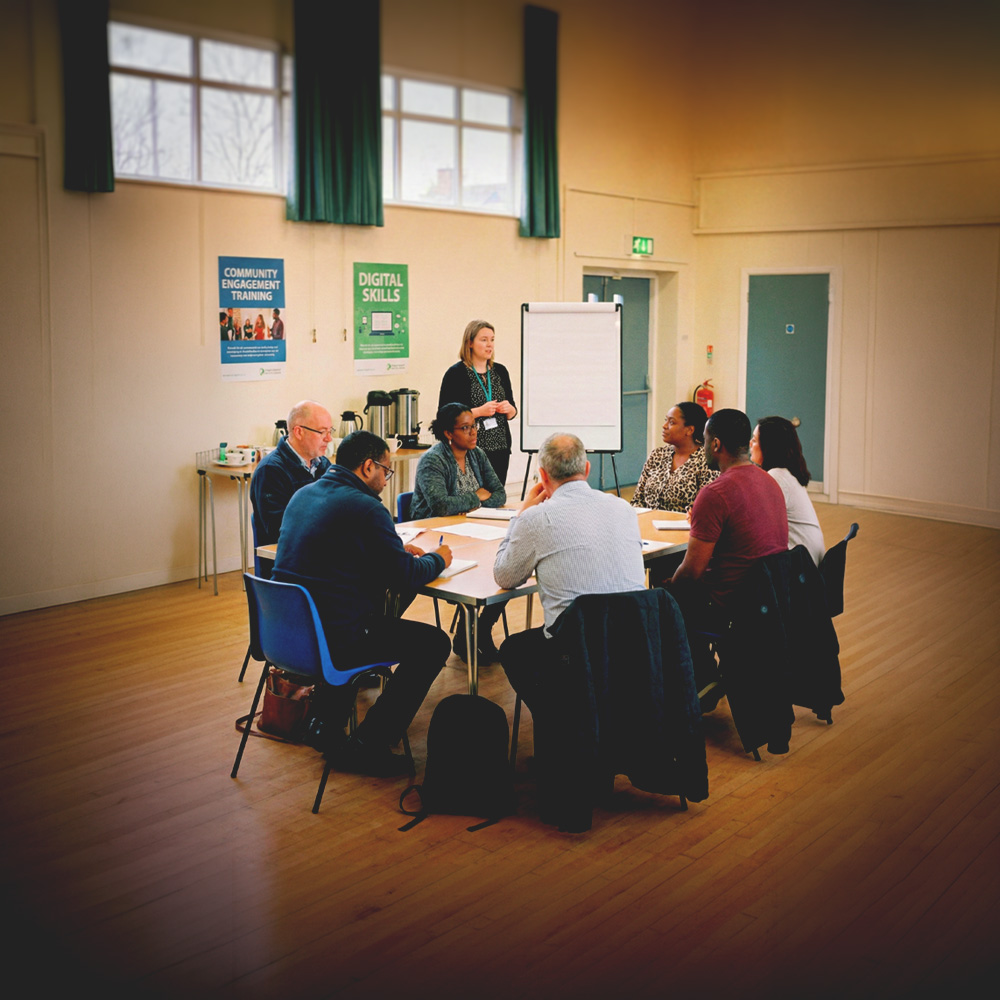 Group of diverse adults sitting around a table in a bright room attending a community engagement and digital skills training session.