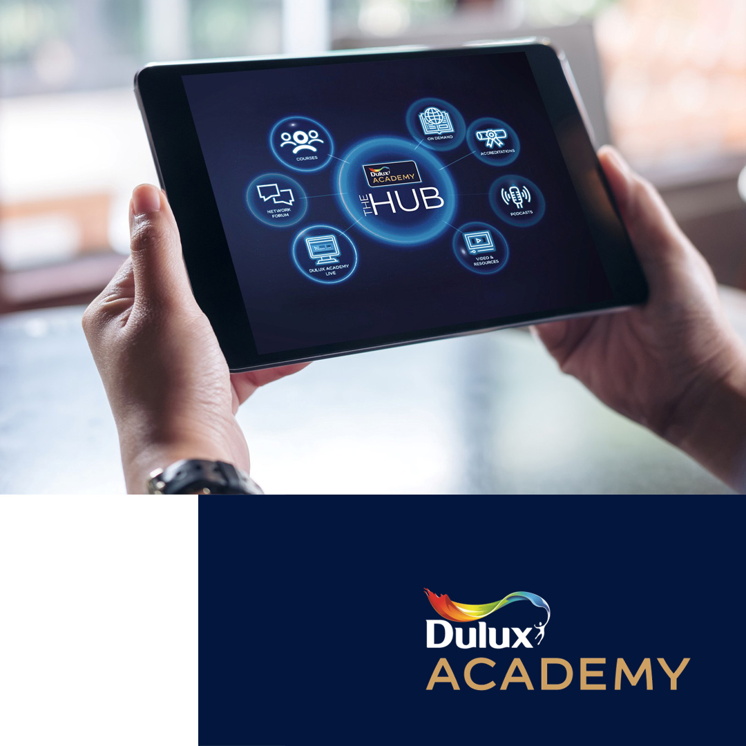 Hands holding a tablet displaying Dulux Academy The Hub interface with icons for courses, network forum, live, on demand, accreditations, podcasts, and video resources.