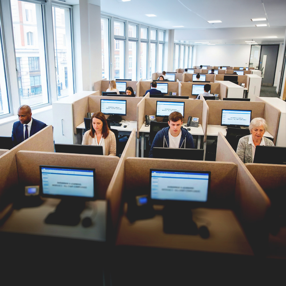 Office with multiple employees sitting in cubicles working on desktop computers.