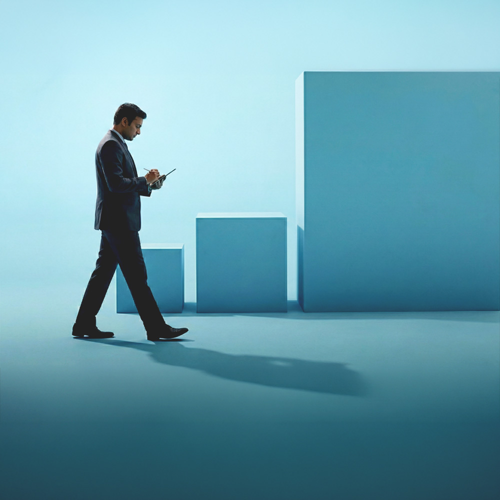 Businessman in a suit walking while writing on a tablet with three ascending blue cubes in the background.